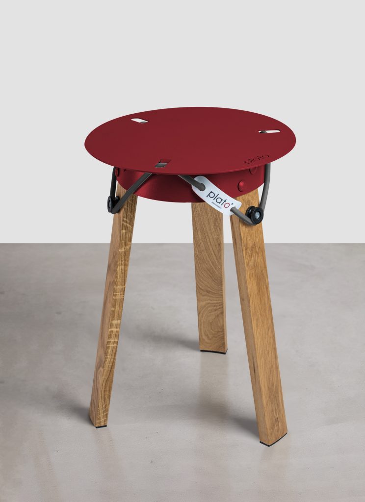 Mini Tabouret Plato® en chêne massif et acier thermolaqué rouge vin, utilisé comme desserte à côté d'un fauteuil